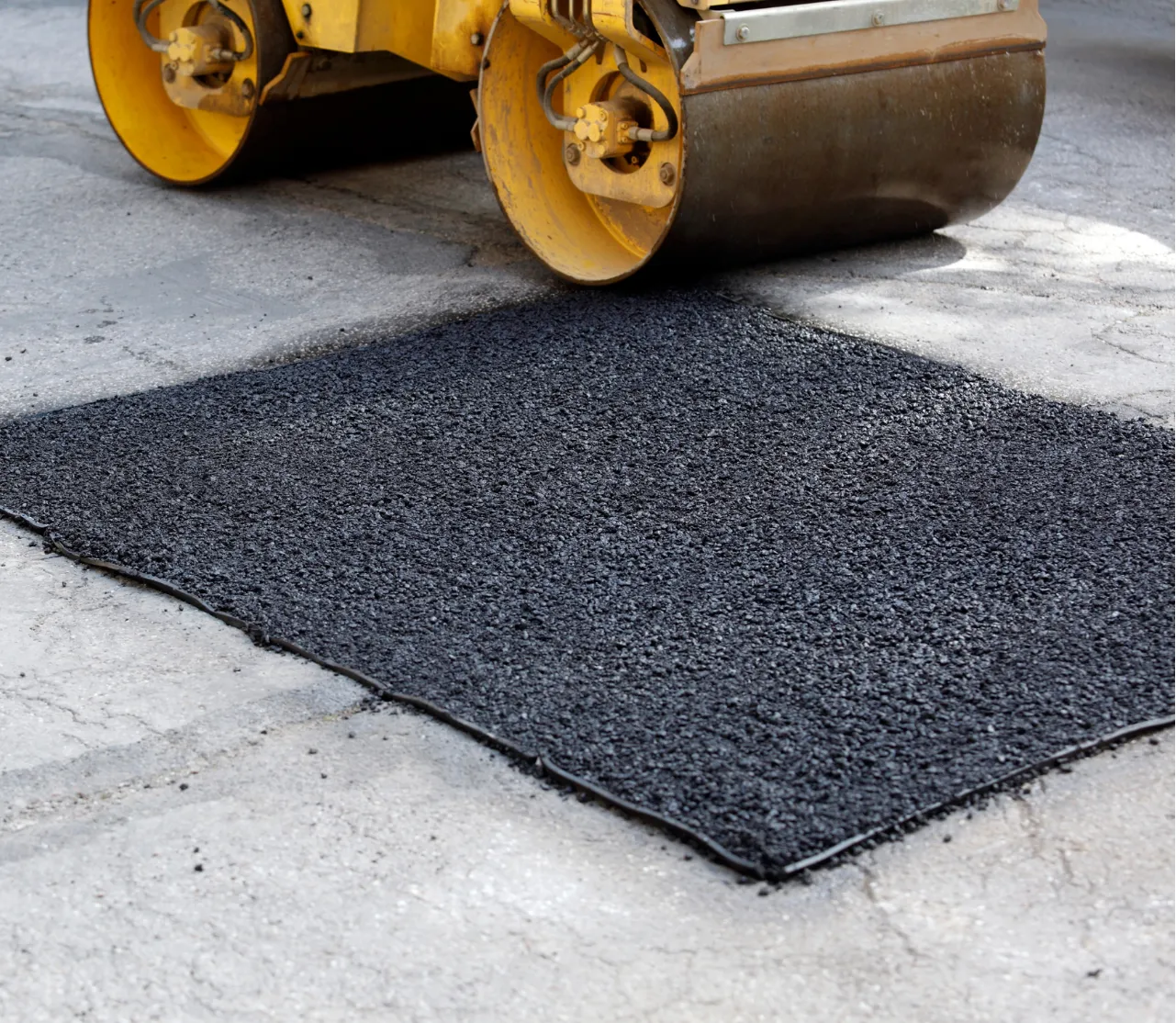 pothole-3 A steamroller compacts fresh asphalt patch on a road during repair work.