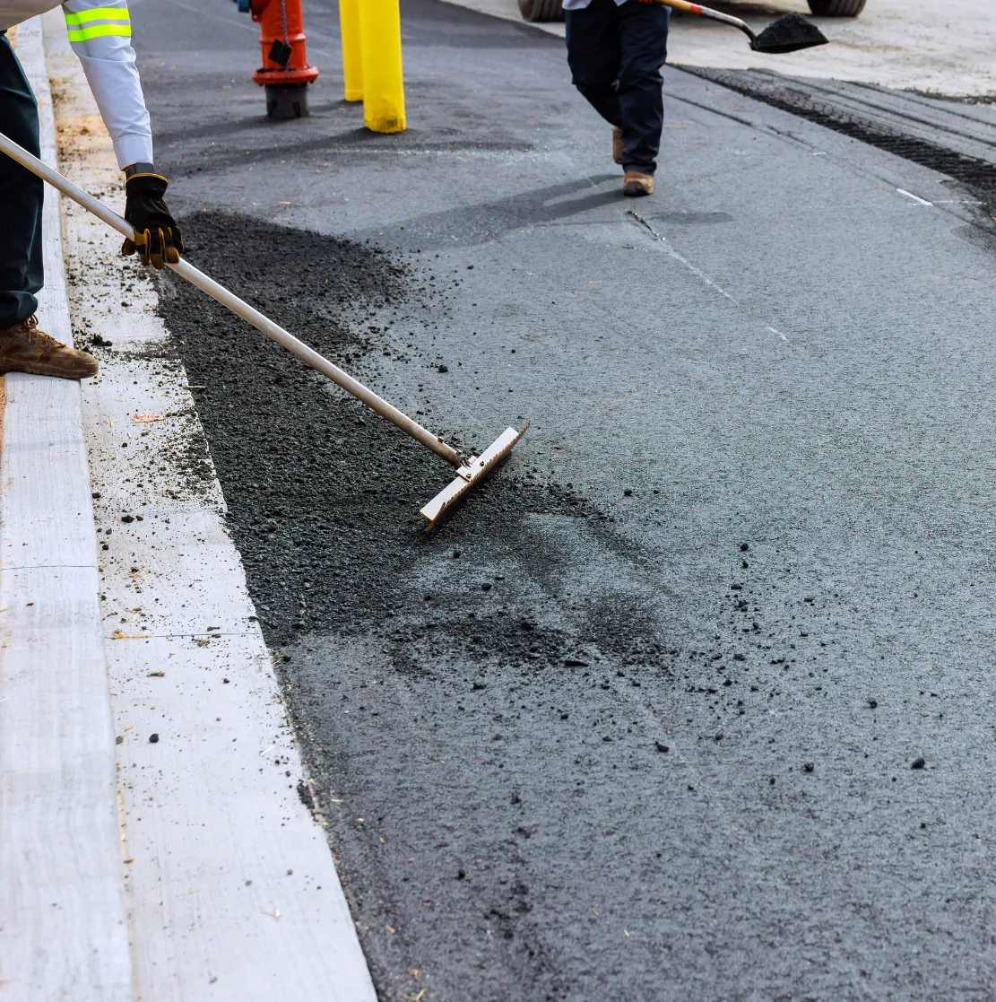 repair-2 Workers spreading fresh asphalt on a road with tools during a street construction project.