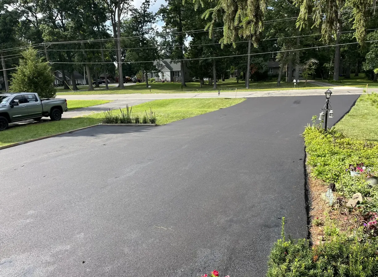 How to Prepare Your Property for a Paving Project_ A Step-by-Step Guide-img Freshly paved asphalt driveway with a green lawn, trees, and a pickup truck parked on the left.